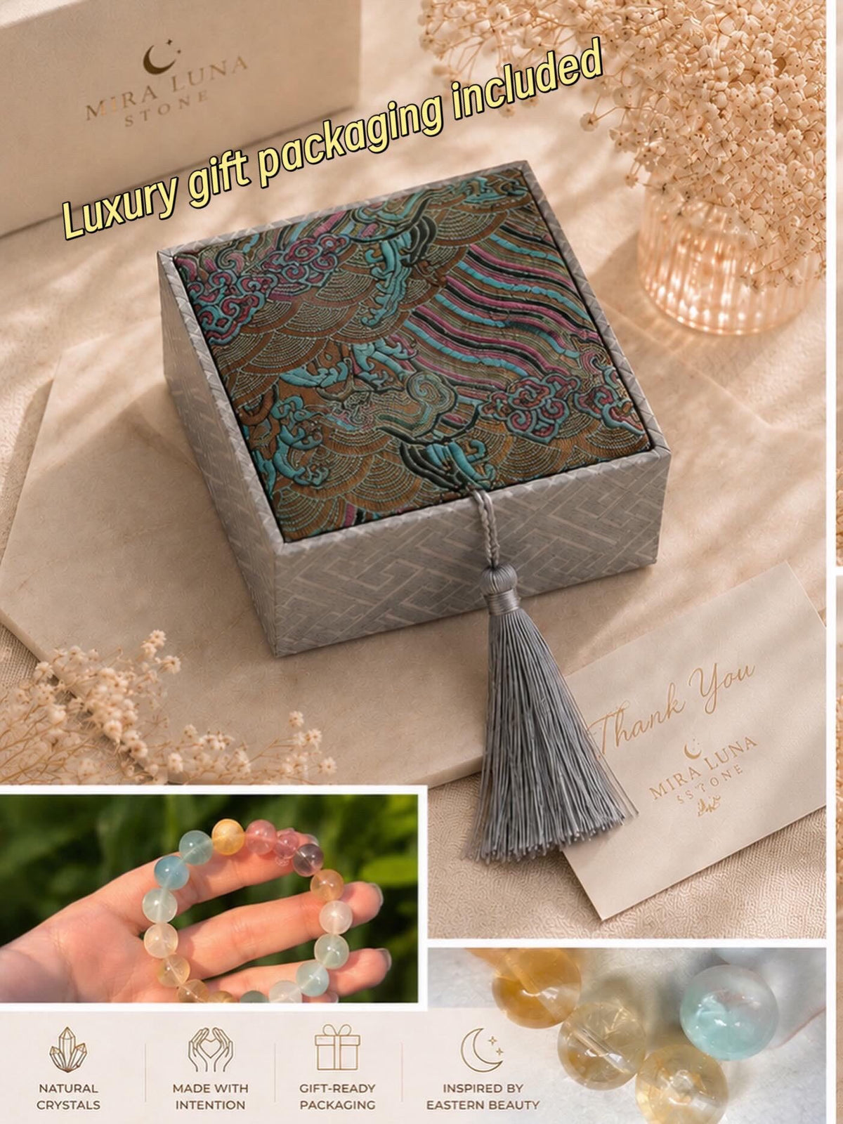 May include: A square gray box with a patterned fabric lid featuring blue, pink, and gold cloud motifs, finished with a gray tassel. The set includes a multi-colored crystal bead bracelet, a thank you card, and a box labeled Mira Luna Stone.